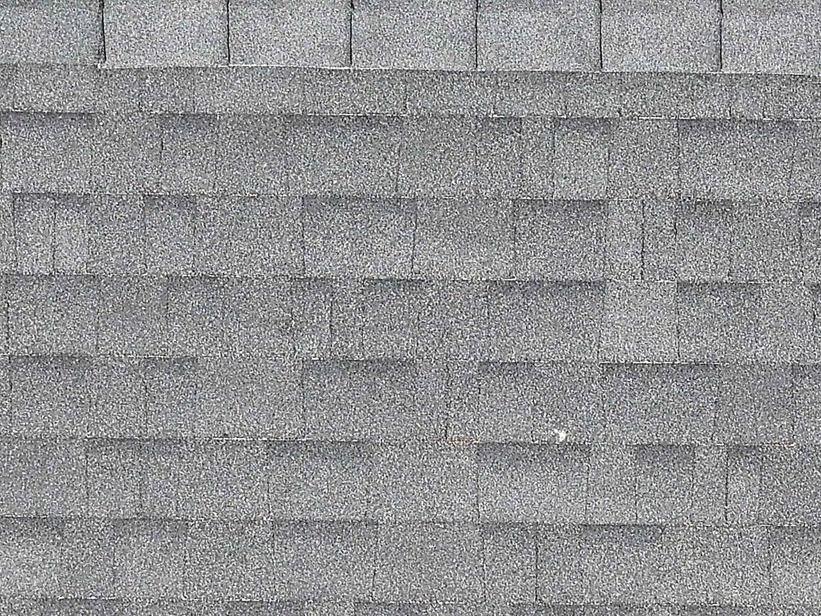 Tight high-resolution drone detail of the shingle field, individual asphalt shingle tabs and granule wear legible.