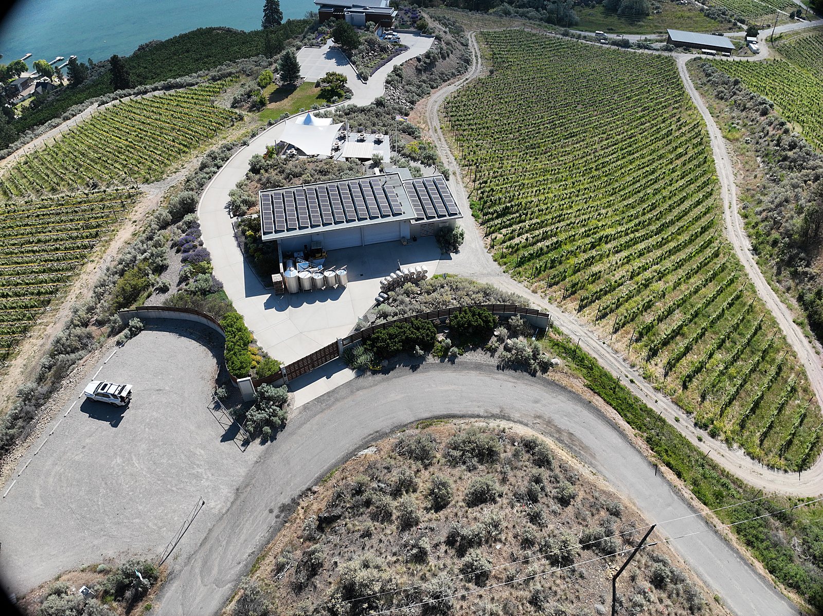 A hillside venue read whole from the air: the buildings, the tent patio, the parking area, and the access lanes in one staged, crowd-free aerial frame.